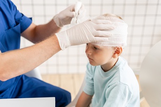 Das Bild zeigt ein Kind, das in der Klinik wegen einer Kopfverletzung verbunden wird